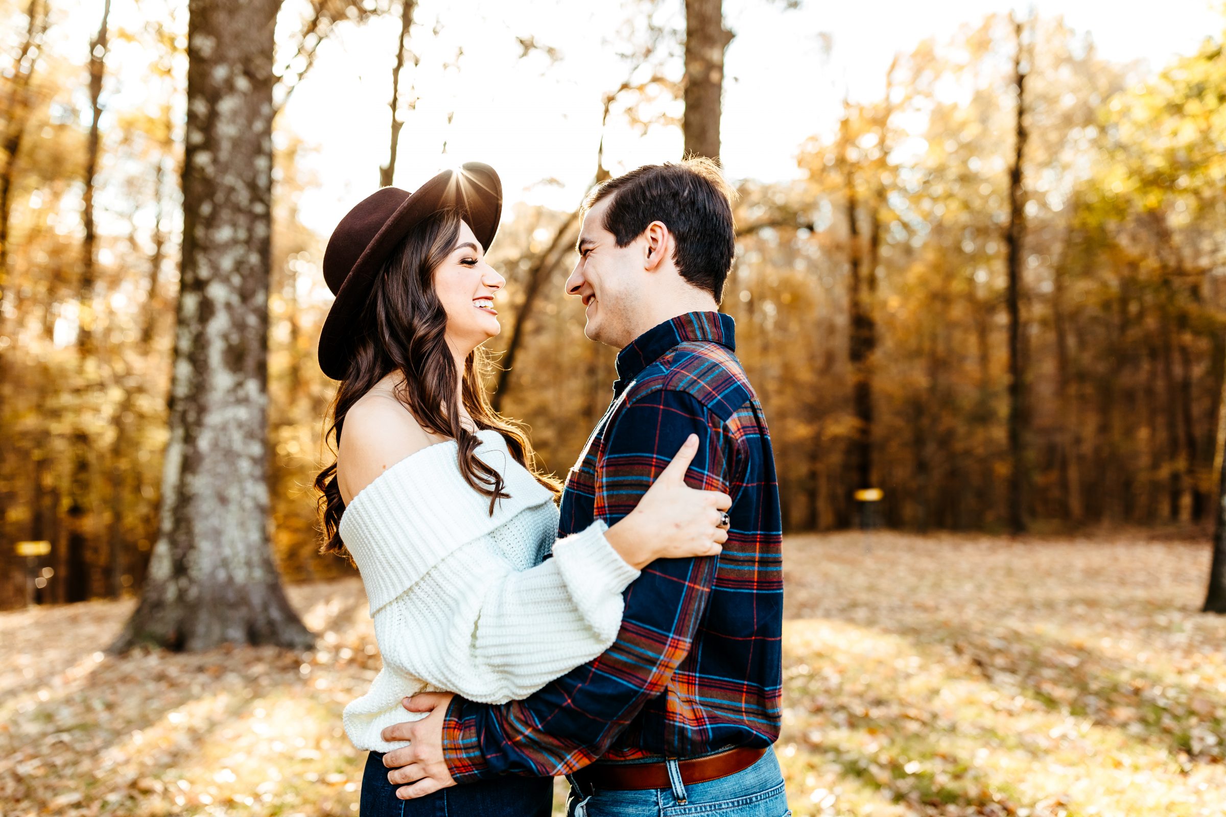 Engaged couple in forest on fall day laughing during sunset